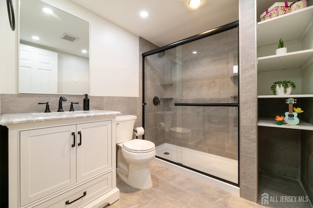 bathroom featuring tile walls, visible vents, toilet, a shower stall, and vanity