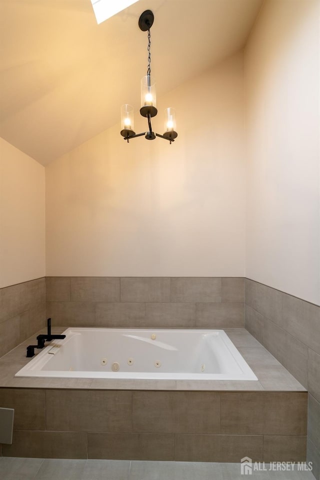 bathroom with a tub with jets, vaulted ceiling, and a notable chandelier