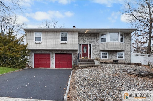 bi-level home featuring aphalt driveway, brick siding, a garage, and fence