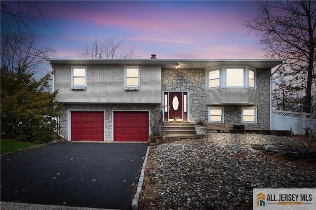 raised ranch with brick siding, driveway, a garage, and fence