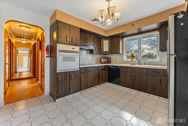 kitchen with a notable chandelier, black appliances, a sink, ventilation hood, and arched walkways