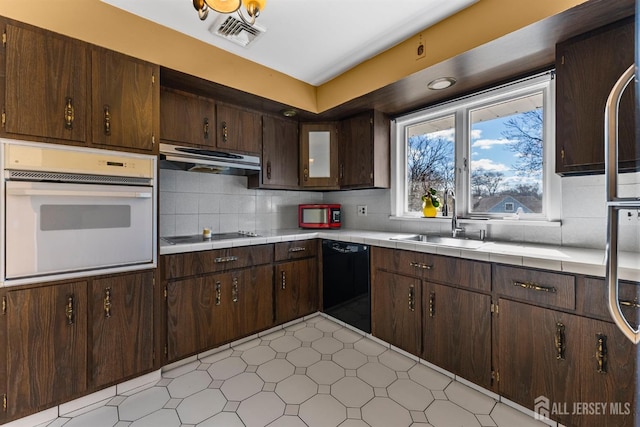 kitchen featuring black appliances, a sink, range hood, dark brown cabinetry, and tile counters