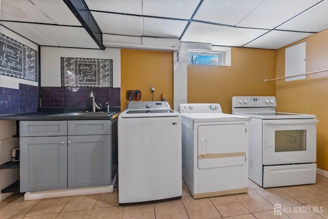 washroom with light tile patterned floors, laundry area, washing machine and dryer, and a sink