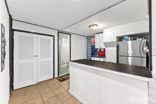 kitchen featuring dark countertops, freestanding refrigerator, a peninsula, white cabinets, and light tile patterned floors