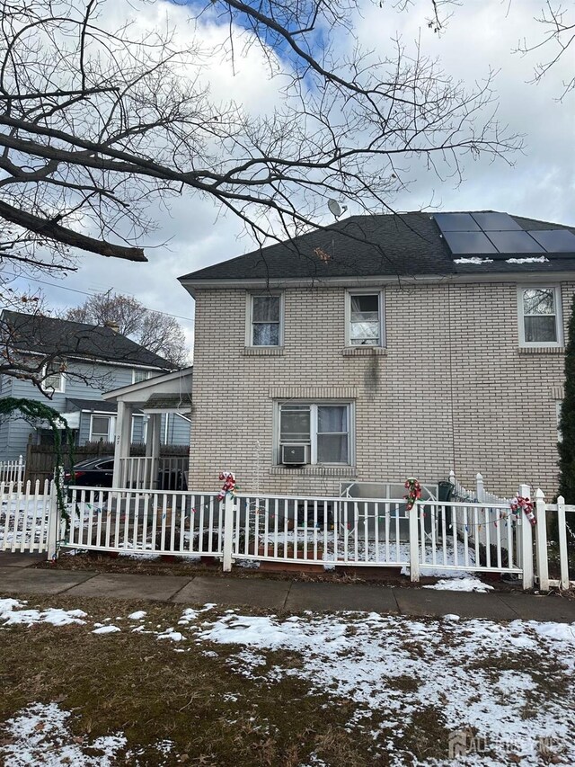 snow covered back of property featuring cooling unit and solar panels