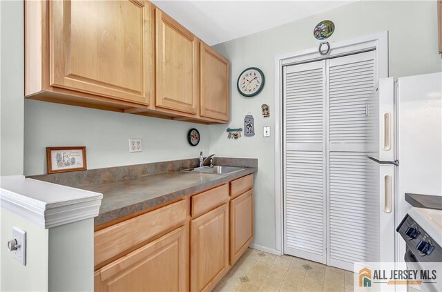 kitchen featuring light tile patterned floors, dark countertops, freestanding refrigerator, light brown cabinets, and a sink