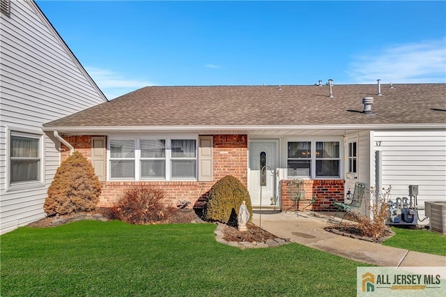 view of front of property with brick siding, central air condition unit, a front yard, and roof with shingles