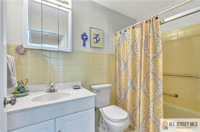 bathroom with a wainscoted wall, tile walls, shower / bath combination with curtain, toilet, and vanity