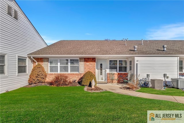 view of front facade with brick siding, roof with shingles, central AC, and a front lawn