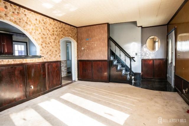foyer featuring a wainscoted wall, arched walkways, wallpapered walls, stairway, and ornamental molding
