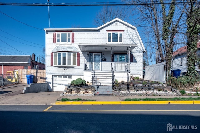 view of front of property featuring a gambrel roof, concrete driveway, an attached garage, fence, and a porch