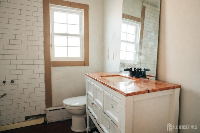 bathroom with a baseboard radiator, toilet, vanity, and a wealth of natural light