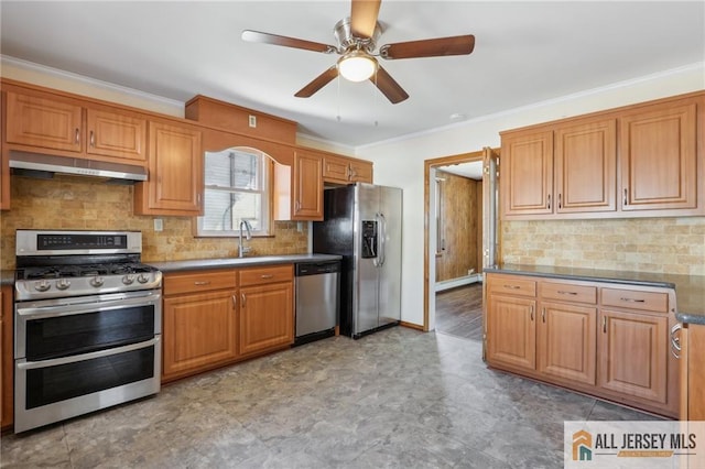 kitchen featuring dark countertops, a sink, appliances with stainless steel finishes, under cabinet range hood, and crown molding