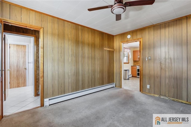 spare room with carpet floors, baseboard heating, wood walls, and a ceiling fan