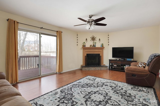 living area featuring a fireplace with raised hearth, a ceiling fan, and wood finished floors