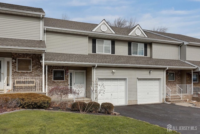 multi unit property featuring an attached garage, a front lawn, roof with shingles, covered porch, and driveway