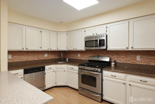 kitchen with light wood-type flooring, a sink, white cabinetry, stainless steel appliances, and decorative backsplash