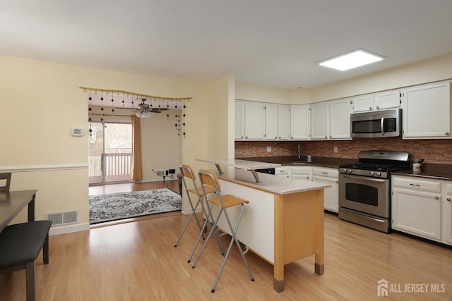 kitchen featuring visible vents, a peninsula, light wood-style flooring, stainless steel appliances, and white cabinets