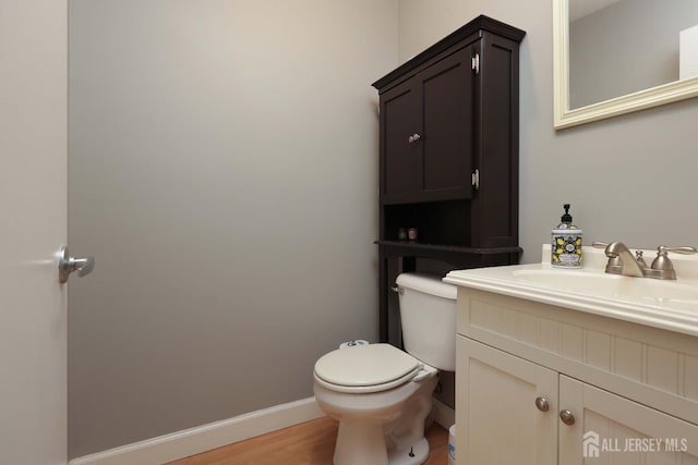 bathroom featuring baseboards, toilet, wood finished floors, and vanity