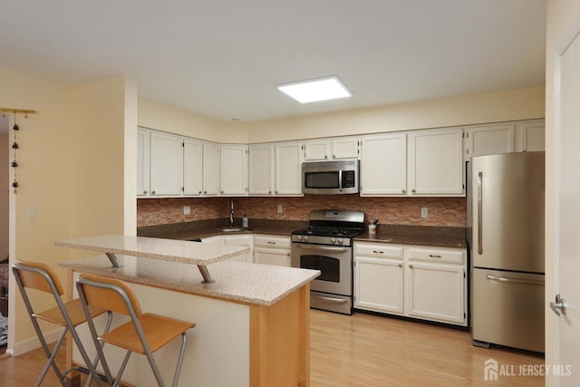 kitchen with decorative backsplash, a peninsula, light wood-style flooring, and stainless steel appliances