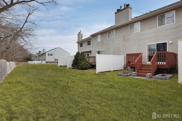 back of house featuring a lawn, a deck, a chimney, and fence