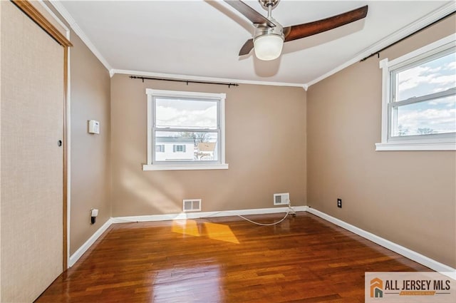 spare room featuring a wealth of natural light, visible vents, crown molding, and wood finished floors