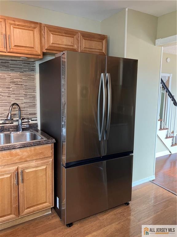 kitchen with light wood-type flooring, decorative backsplash, a sink, and freestanding refrigerator