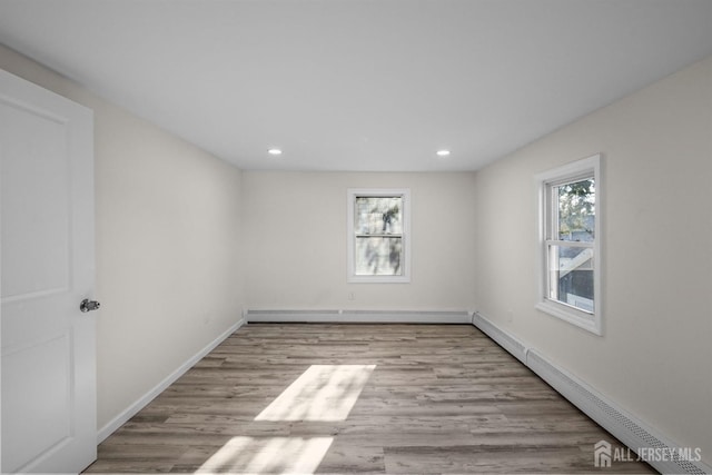 unfurnished room featuring a baseboard heating unit, baseboards, and light wood-style floors