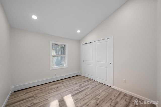 unfurnished bedroom featuring a baseboard radiator, a closet, light wood-style floors, vaulted ceiling, and baseboards