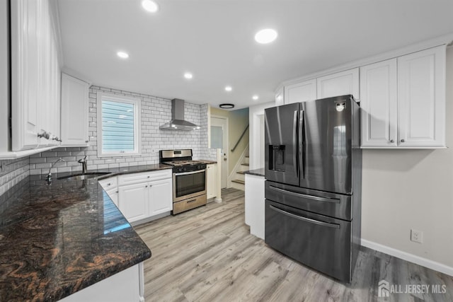 kitchen featuring sink, appliances with stainless steel finishes, white cabinetry, dark stone counters, and wall chimney exhaust hood