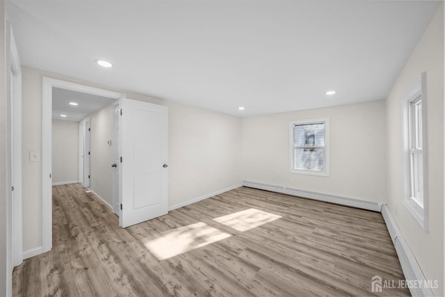 spare room with a baseboard heating unit, light wood-style flooring, and baseboards