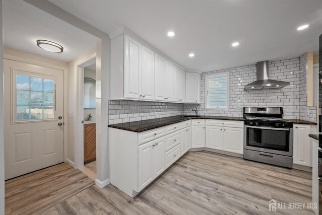 kitchen featuring white cabinetry, light wood-style floors, wall chimney range hood, stainless steel gas stove, and plenty of natural light