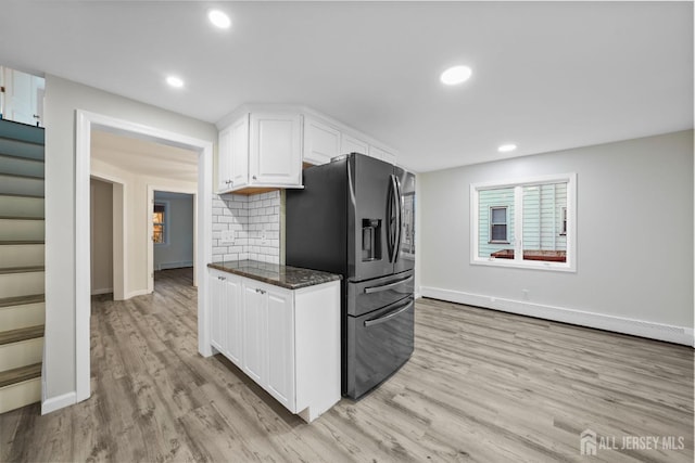 kitchen featuring white cabinets, light wood-type flooring, decorative backsplash, dark stone countertops, and stainless steel fridge