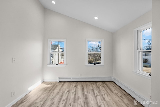 spare room with lofted ceiling, a baseboard radiator, light wood-style flooring, and a wealth of natural light