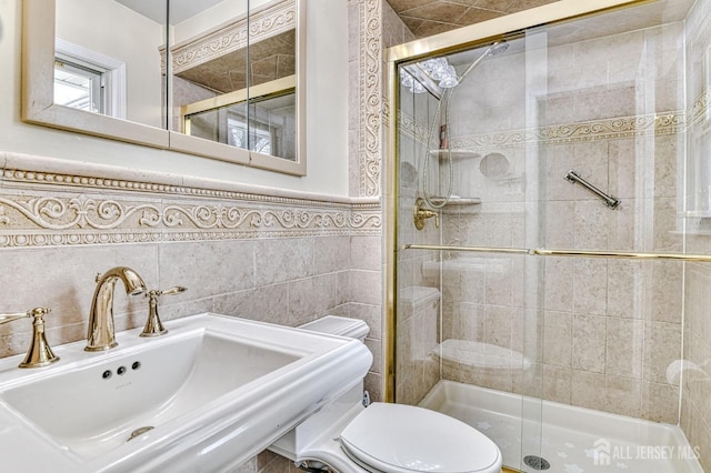 full bathroom featuring a sink, a shower stall, wainscoting, tile walls, and toilet