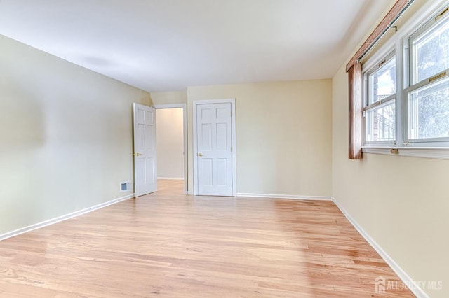 unfurnished room featuring visible vents, light wood-type flooring, and baseboards