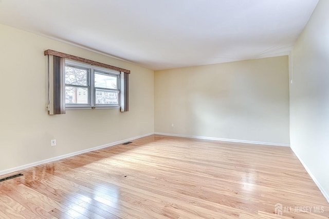 empty room with visible vents, light wood-style flooring, and baseboards