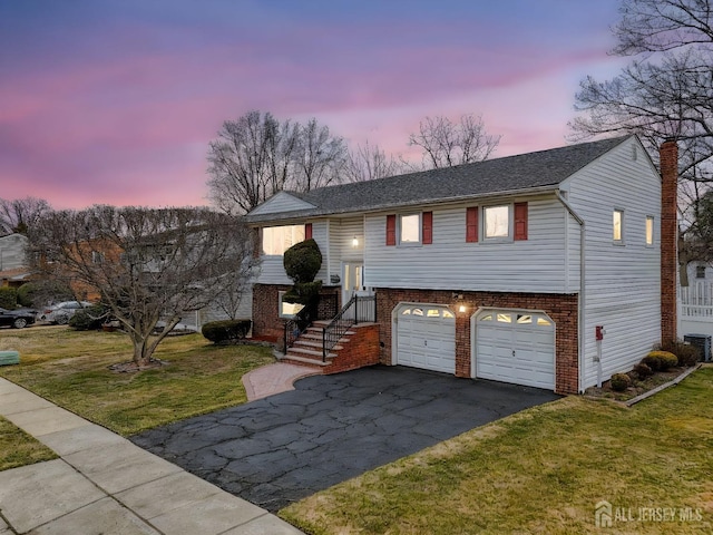 bi-level home with a chimney, a garage, aphalt driveway, a lawn, and brick siding