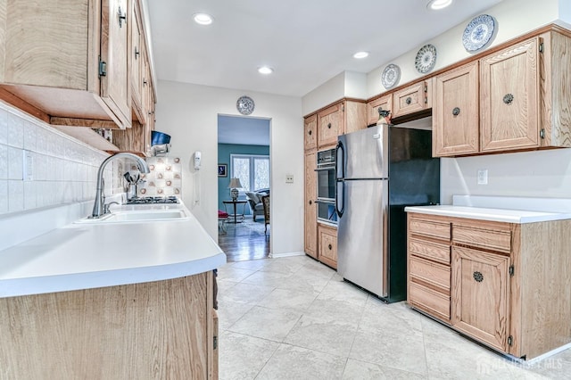 kitchen featuring oven, a sink, freestanding refrigerator, light countertops, and decorative backsplash