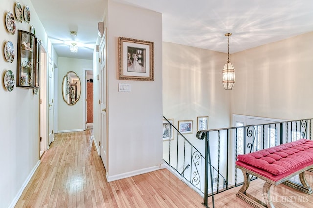 hall featuring light wood-style flooring, an upstairs landing, baseboards, and a chandelier