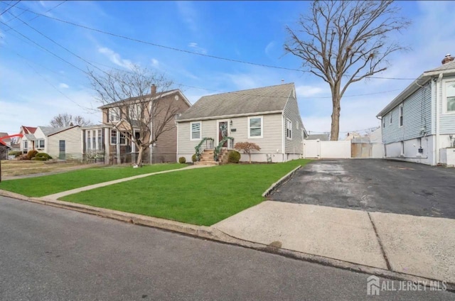 view of front facade featuring aphalt driveway, fence, and a front lawn