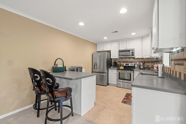 kitchen featuring stainless steel appliances, a sink, crown molding, white cabinets, and a kitchen bar