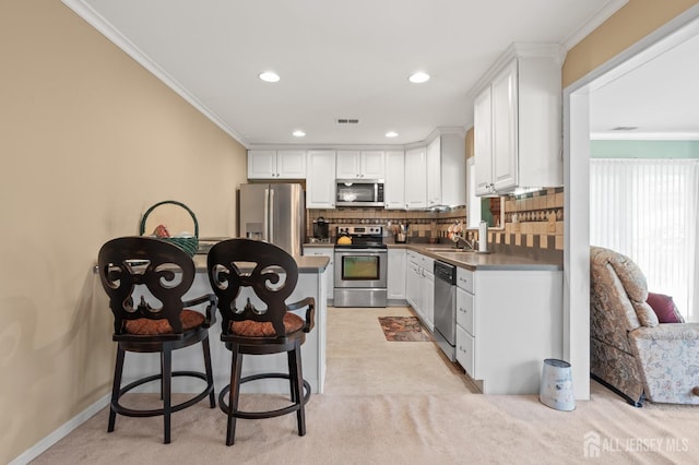 kitchen featuring stainless steel appliances, white cabinetry, a sink, tasteful backsplash, and ornamental molding