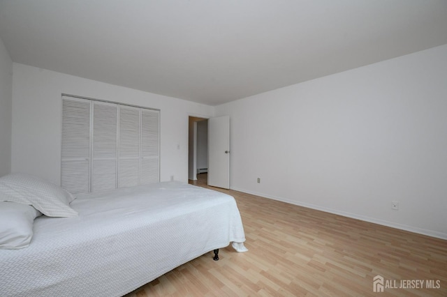 bedroom with light wood-style flooring, a closet, baseboards, and a baseboard heating unit