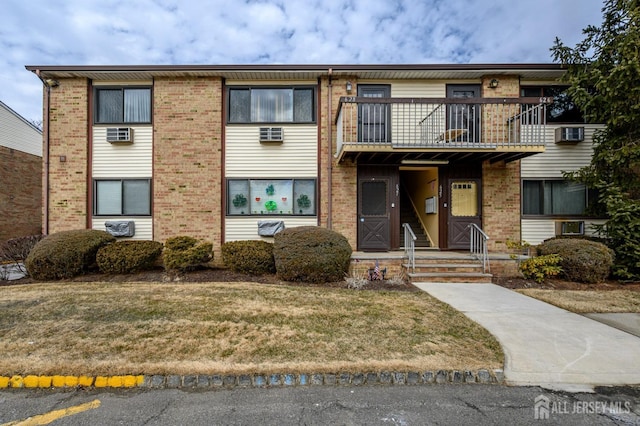 view of front facade with a balcony, brick siding, and a front lawn