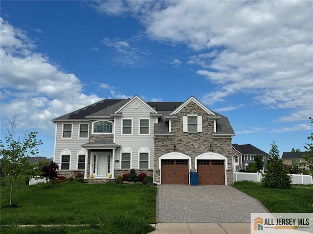 view of front of property with stone siding, roof mounted solar panels, decorative driveway, and a garage