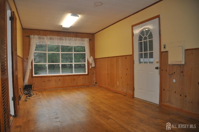 foyer with electric panel, a wainscoted wall, wooden walls, and wood finished floors