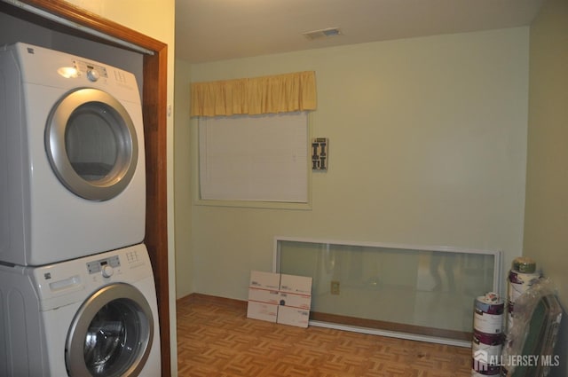 clothes washing area featuring laundry area, stacked washing maching and dryer, and visible vents