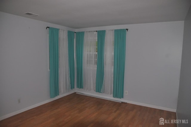 unfurnished room featuring visible vents, wood finished floors, and baseboards