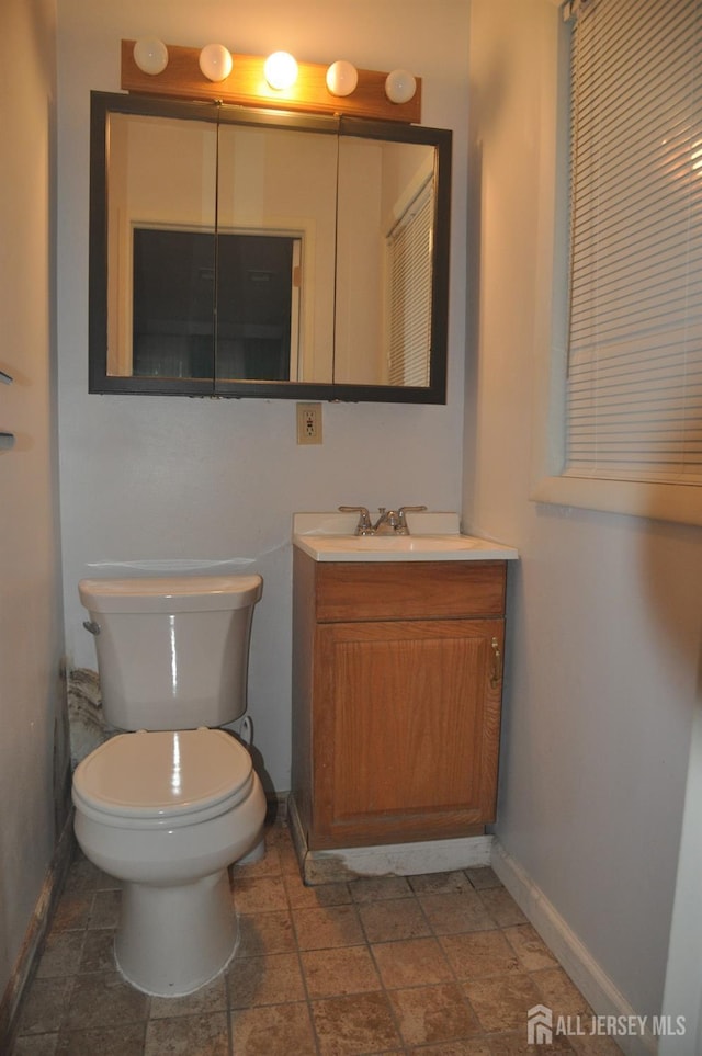 half bath with toilet, baseboards, vanity, and stone finish flooring